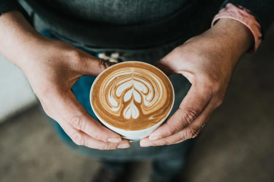 Deux mains autour d'une tasse de café à la mousse dessinée